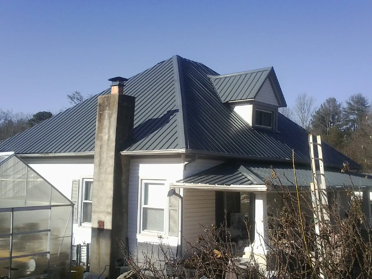 Dark blue standing seam metal roof on a white farmhouse with dormer — Slate & Tile Roof Repair by Roofing Brothers in Wisdom