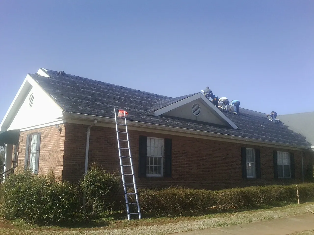 Crew tearing shingles off a brick ranch roof with a ladder set — Emergency Roof Repair work by our crew in Wisdom
