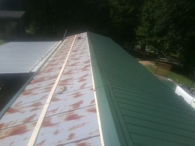 Old rusted panels beside newly installed green metal roofing — Wind Damage Roof Repair by Roofing Brothers in Wisdom