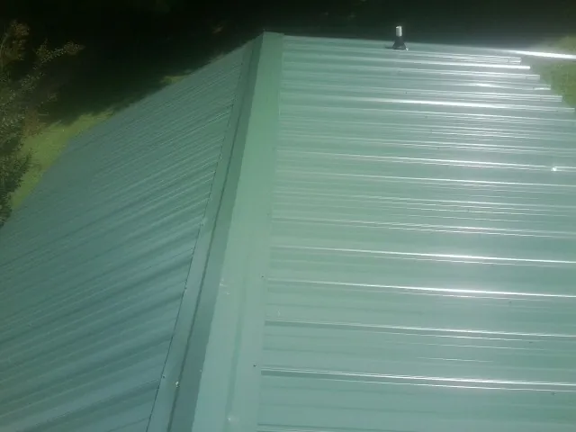 New green metal panels meeting at the ridge of a roof — Flat Roof Repair work by our crew in Wisdom