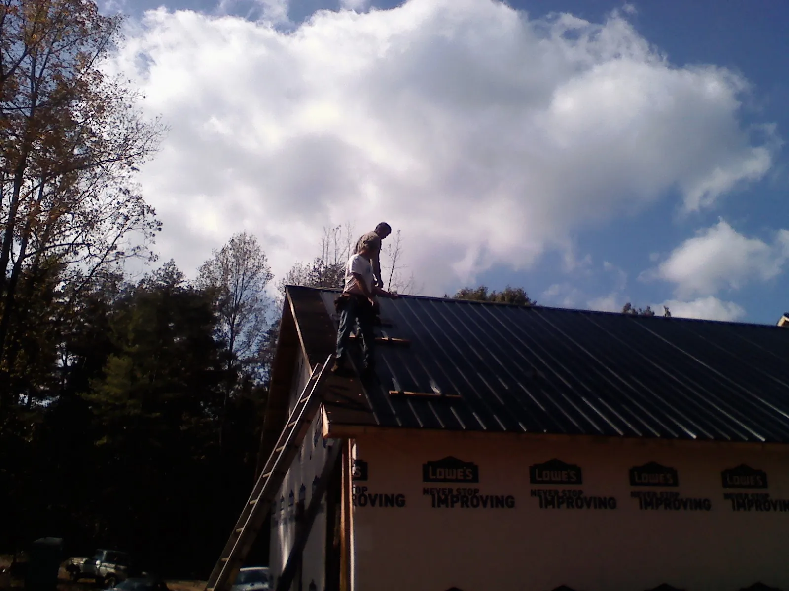 Roofer fastening dark metal panels high against a cloudy sky, from a Roof Inspection job in Wisdom