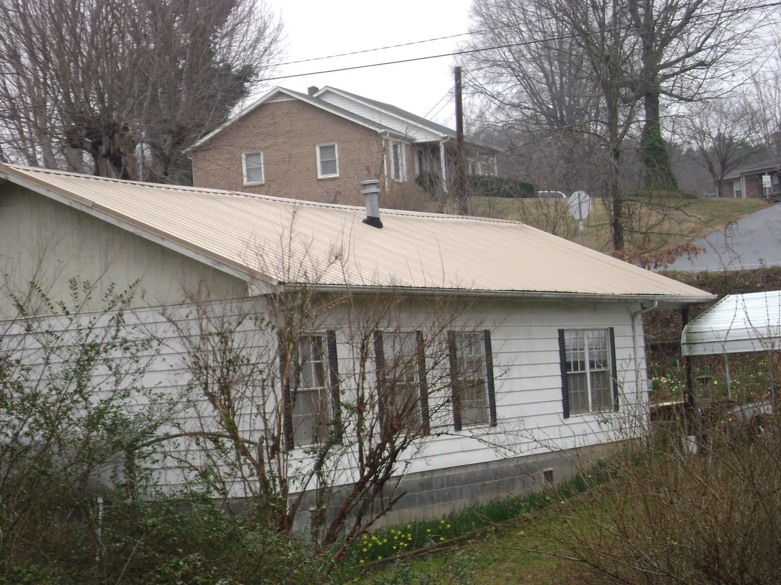 Tan metal roof on a white sided house set into a hillside — Commercial Roofing by Roofing Brothers in Wisdom